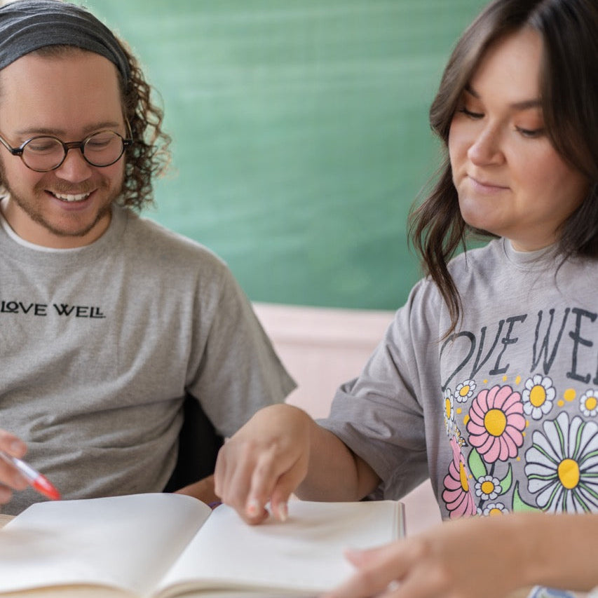 Two people sitting at a table with books and notebooks, one wearing a 'Live Well' shirt.