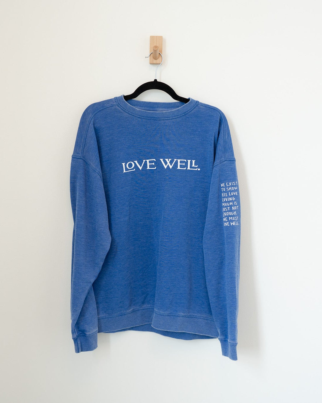 Blue sweatshirt with 'LOVE WELL' text on a white background
