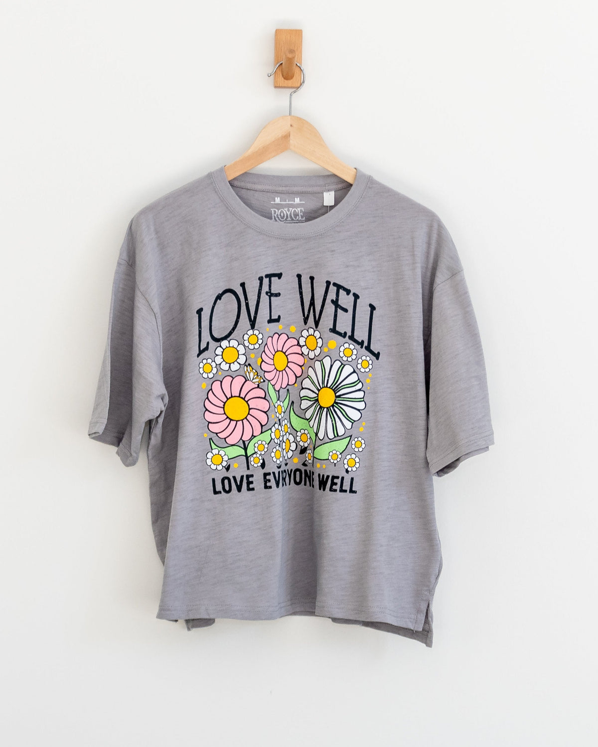 A grey boxy tee with a floral and text graphic on the front, displayed on a hanger against a white background.